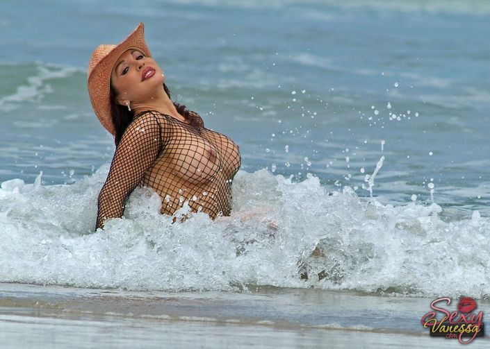 Похотливая особа женского пола в шляпе и сетчатом боди целует болт на берегу моря